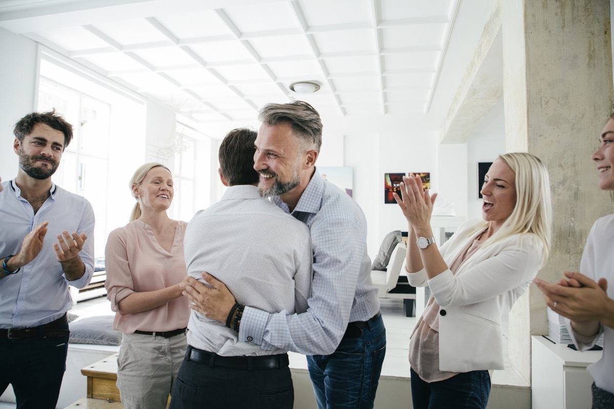 An office team are celebrating together, embracing and applauding each other after a successful business pitch.