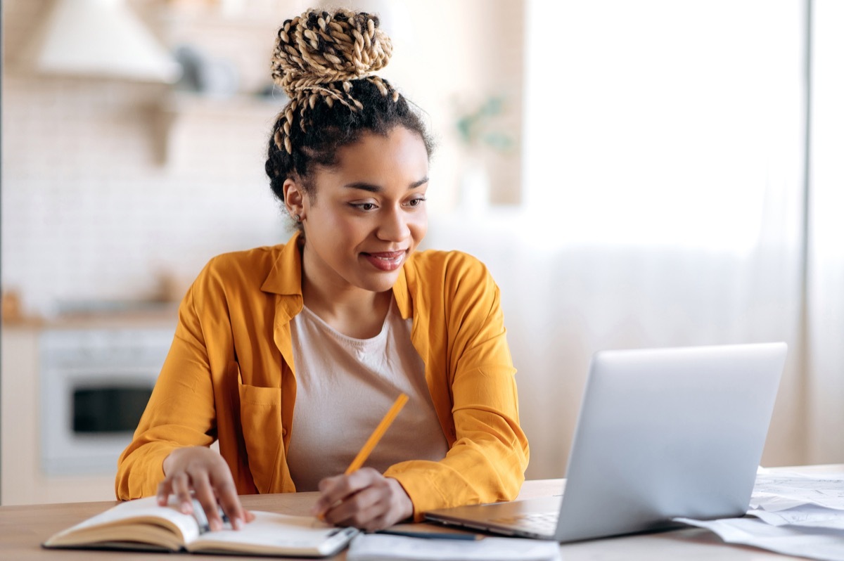 how to become a travel agent - woman taking notes in a notebook while on her laptop