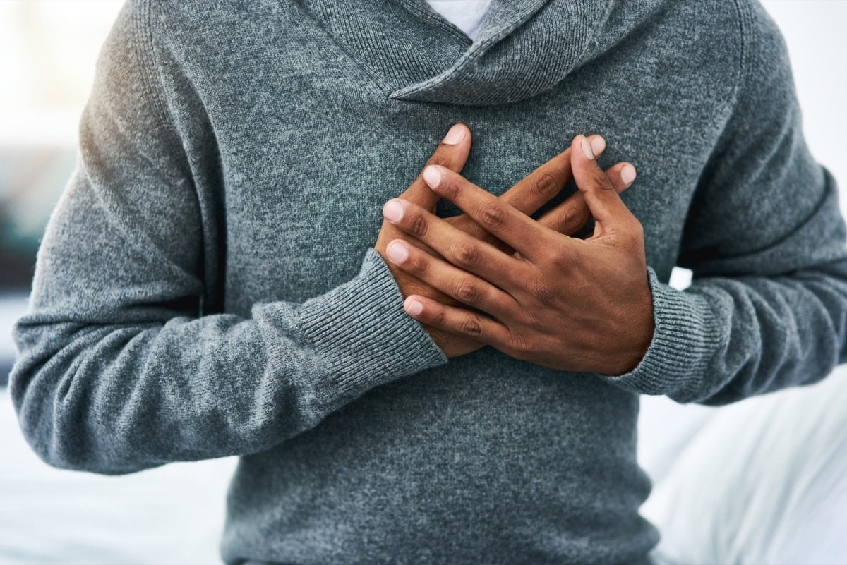 cropped shot of an unrecognizable man holding his chest in pain while sitting on the bed at home