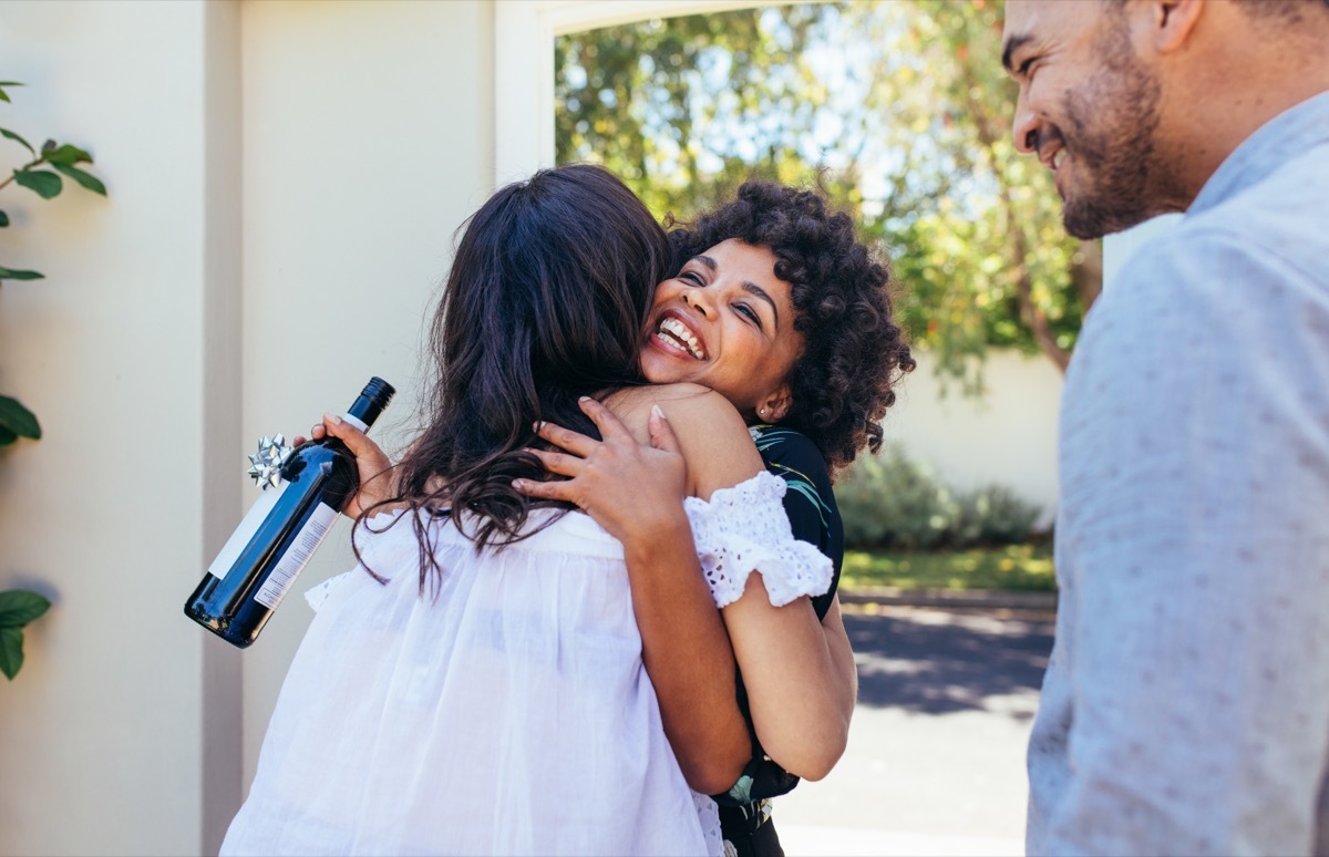 Black woman with natural hair hugs female friend at door with housewarming wine in hand how to live to 100