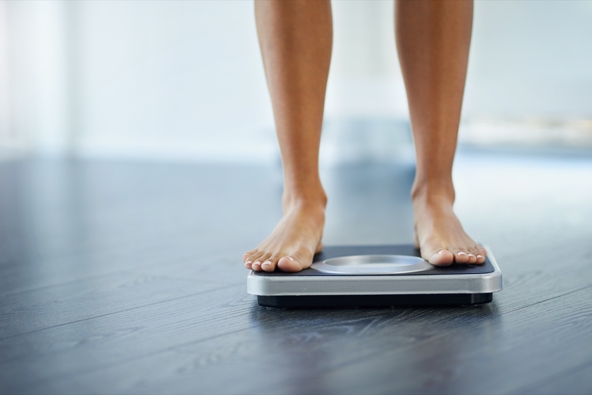 Shot of an unrecognizable woman weighing herself at home