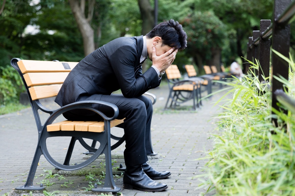 asian man in a suit sitting on a bench with his head in his hands