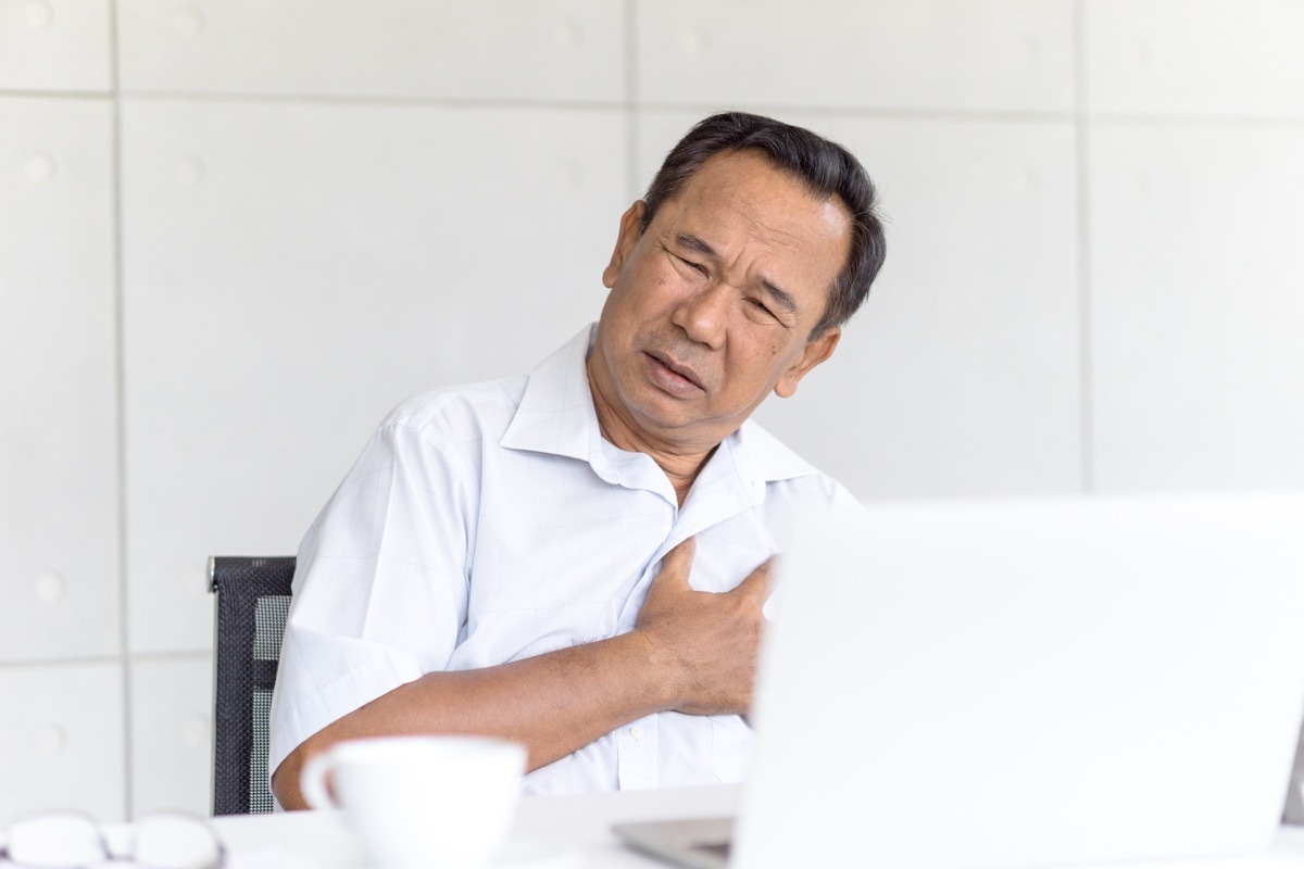 Man sitting at a desk clutching his heart and chest in pain