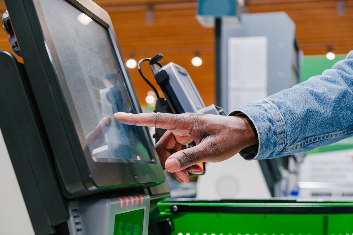 man finger touches screen of self-pay point to pay in shopping mall supermarket light hall extreme close view