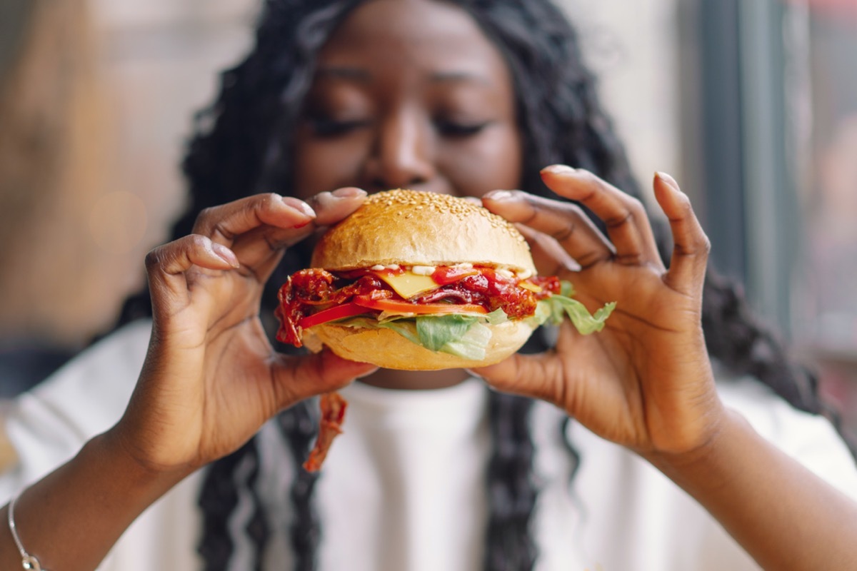 African woman with afro hair eating a tasty classic burger with fries. Cheat Meal.