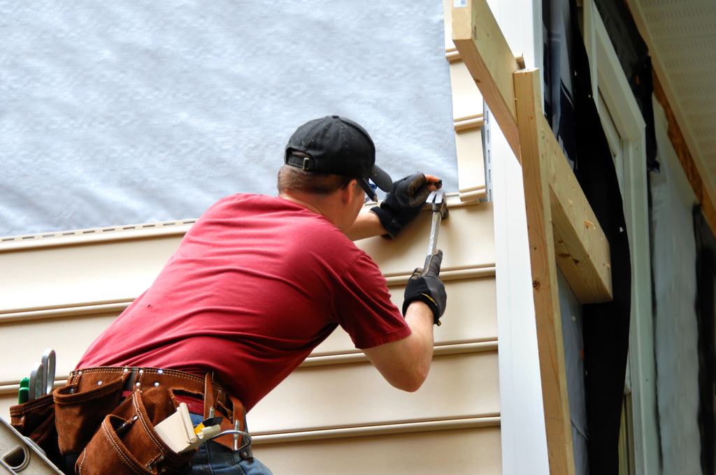 white man in red shirt installing tan siding