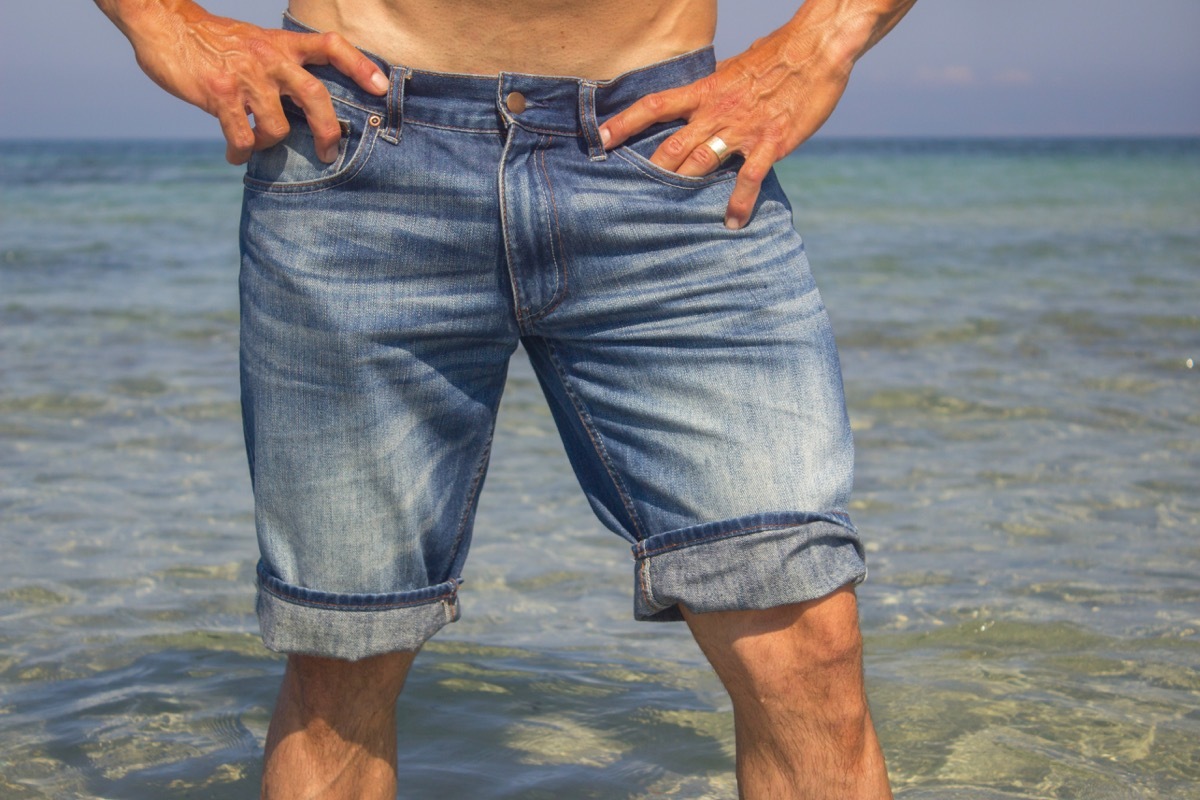 Man wearing jeans shorts standing in the sea water, legs closeup 