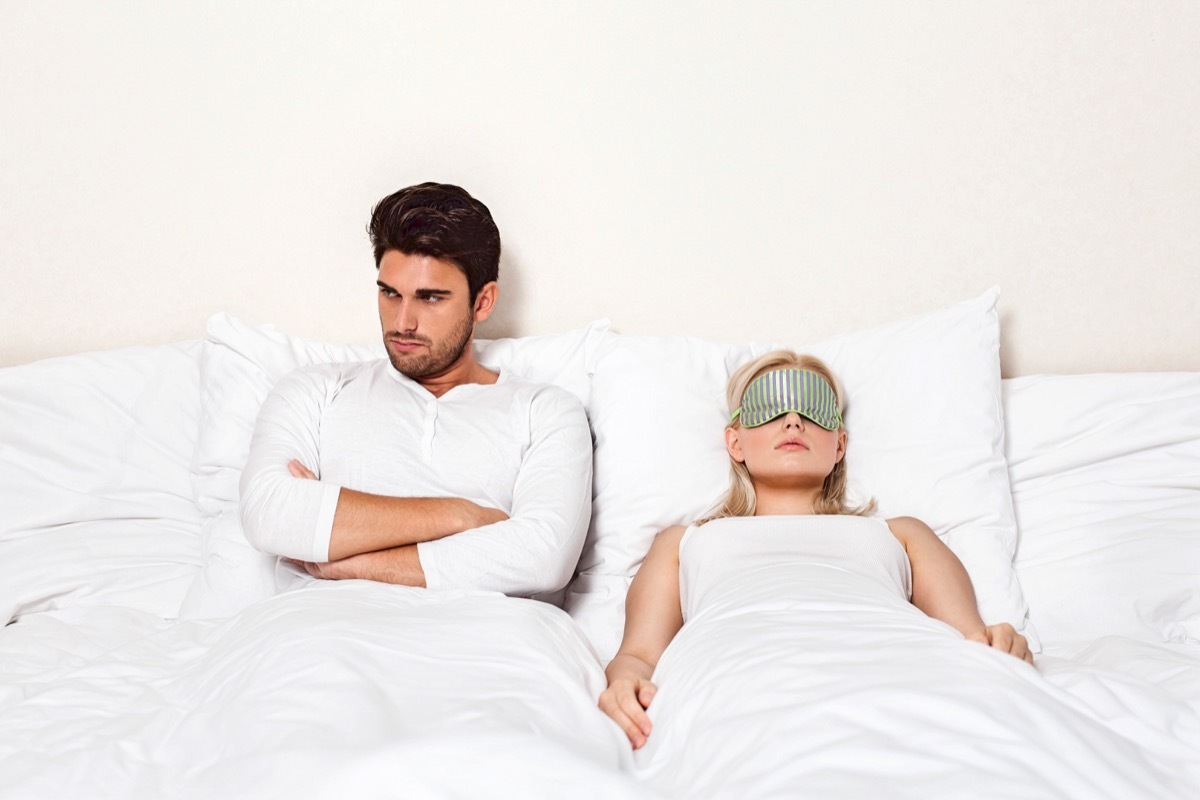 Angry young man with woman sleeping in bed