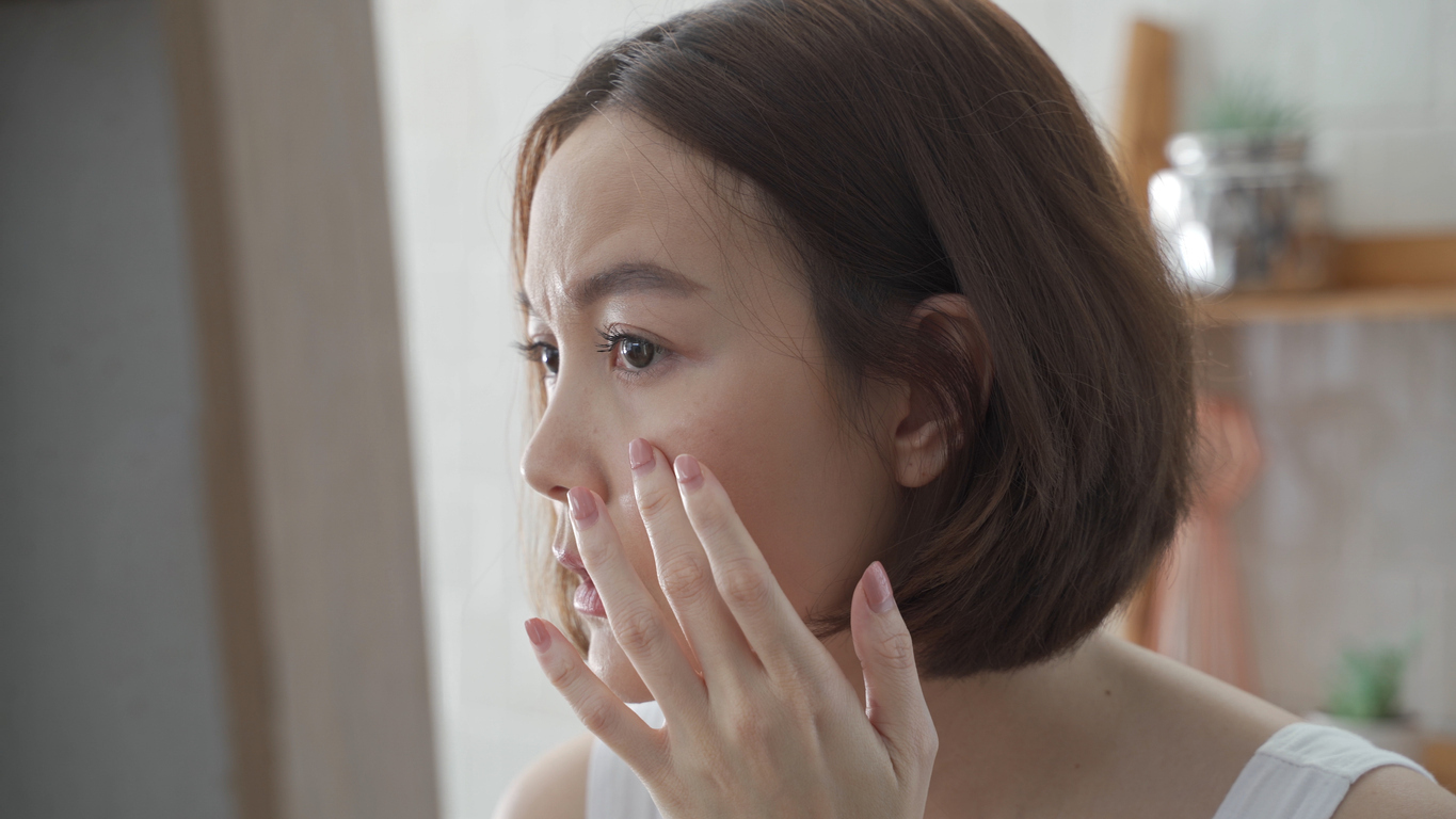 Concerned woman looking at her skin in a mirror.