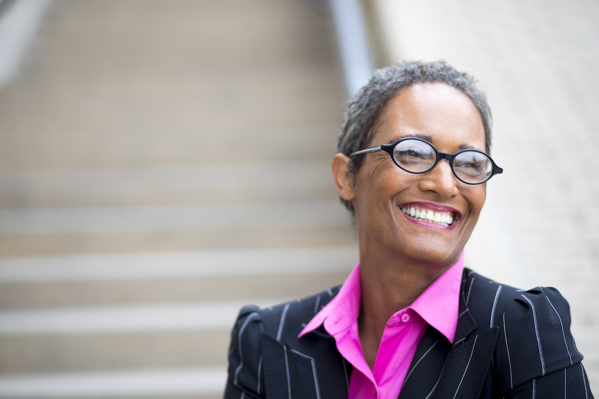 An older businesswoman with short gray hair and a magenta shirt under navy blazer