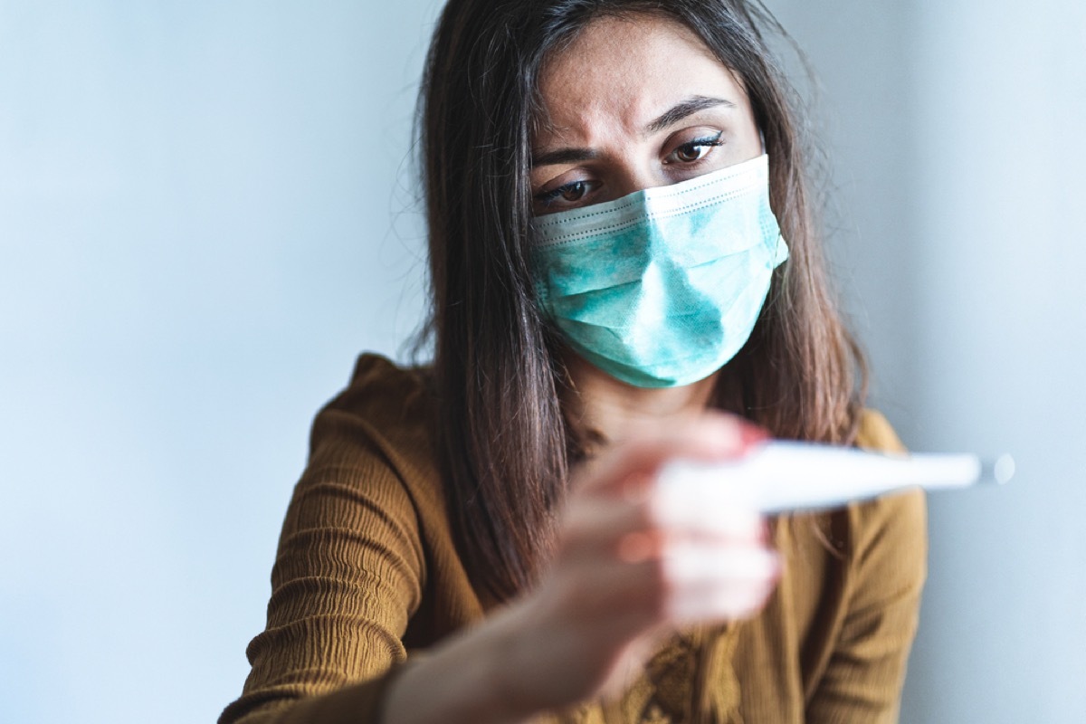 woman with face mask looking at thermometer