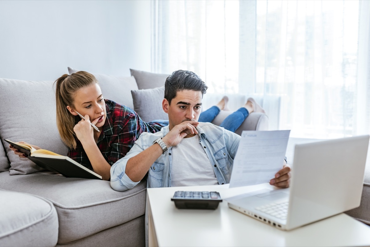 Photo of Depressed young couple doing their accounting in their living room during the day. Young couple calculating their domestic bills at home. Family budget and finances. Young woman doing accounts together with her husband at home, planning new purchase. Serious female making necessary calculations.