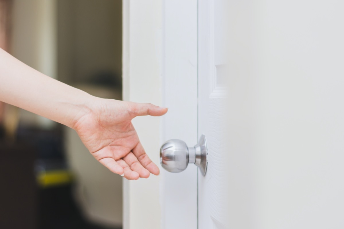 close up of woman's hand reaching to door knob, opening the door