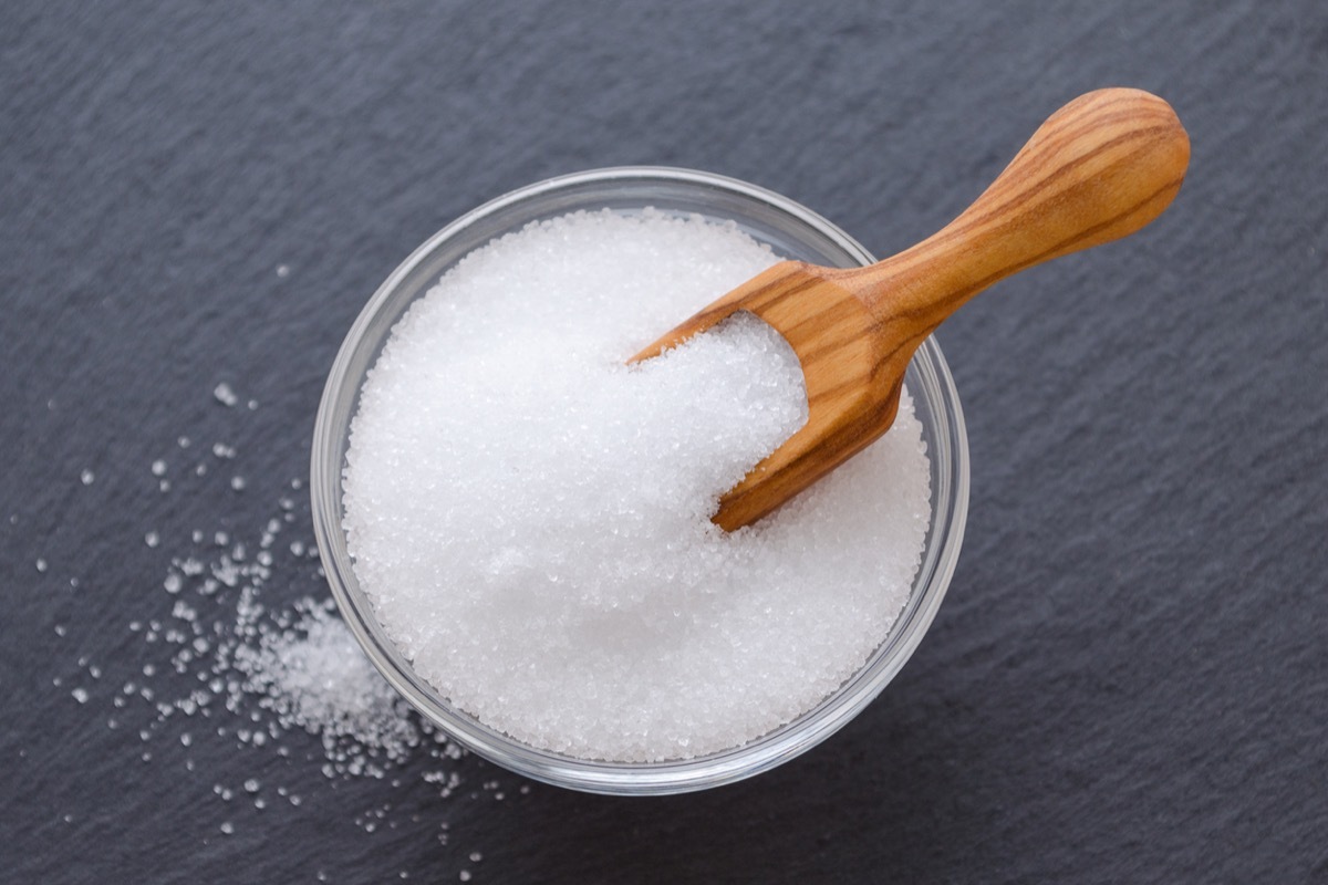 birch sugar xylitol in a wooden scoop and glass bowl on black background closeup