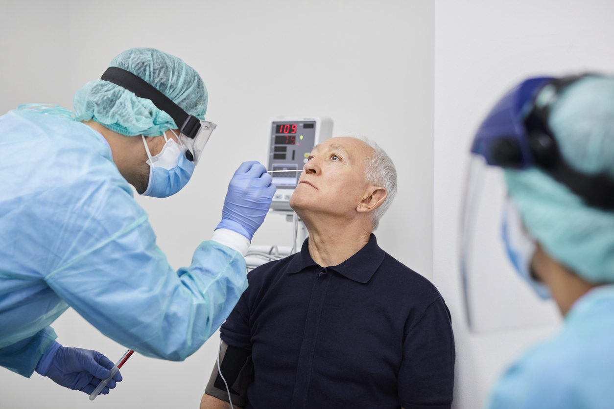 A older man in a blue short has his nose swabbed by a health care worker in full protective gear for a coronavirus test