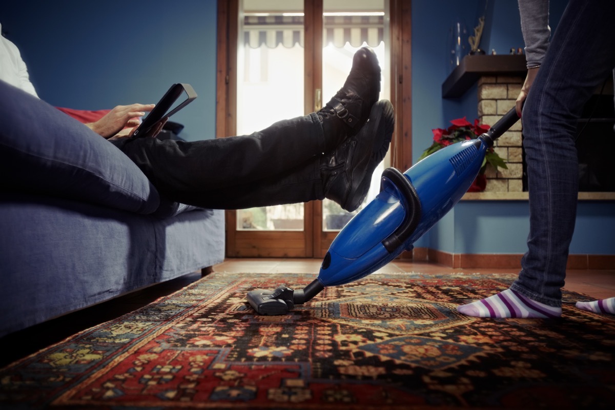 Woman cleaning the house while husband lounges