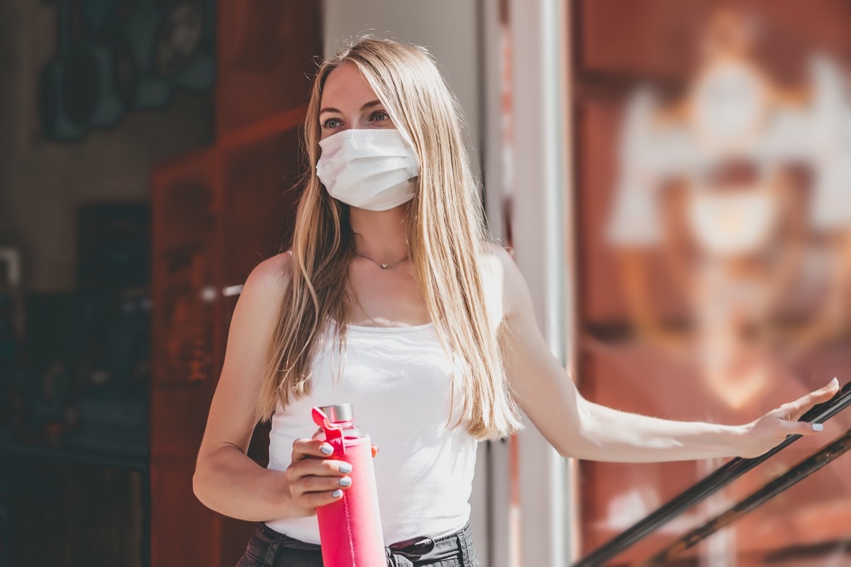 A woman comes out of the cafe door onto the street and holds a water bottle.