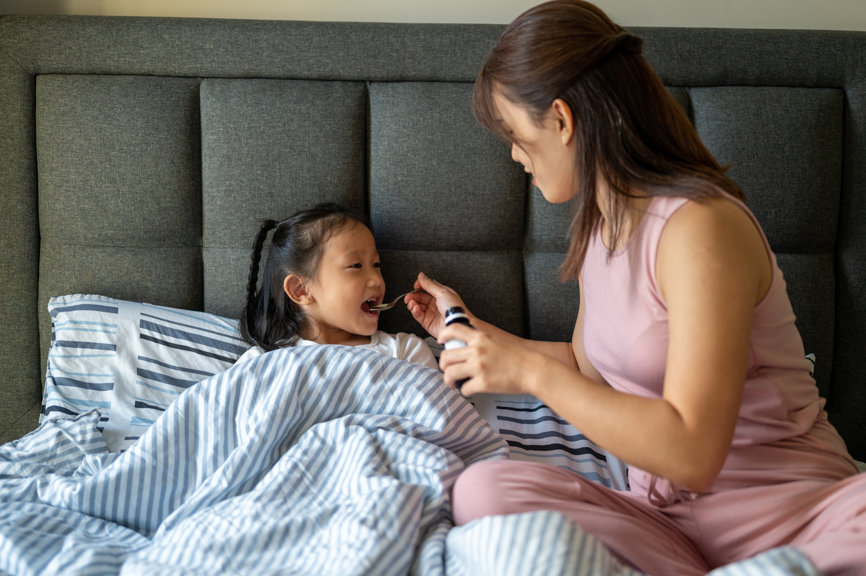 Mom pouring medicine into a spoon for her child.