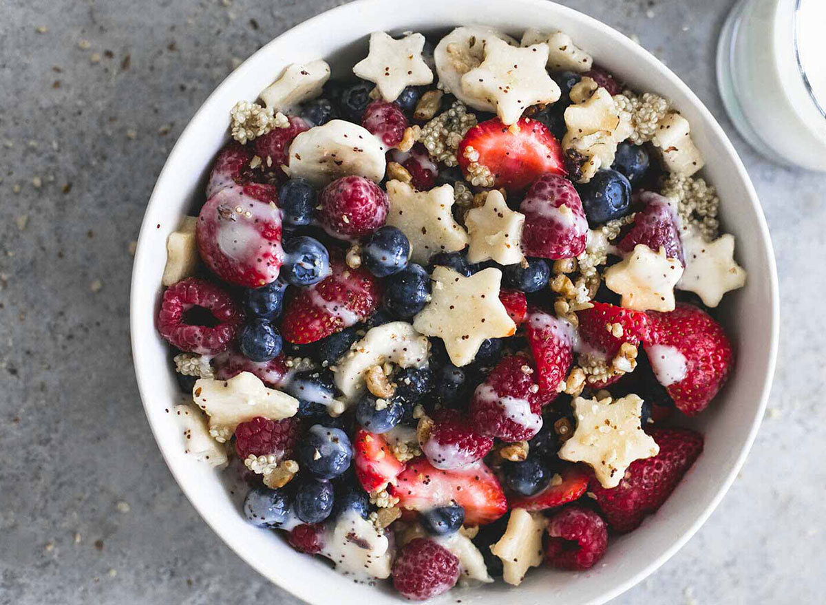 fruit salad with strawberries, blueberries, star shaped apple slices and quinoa in a white bowl on gray background