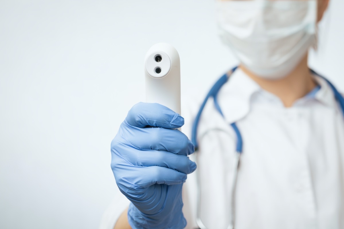 Woman in mask holding thermometer