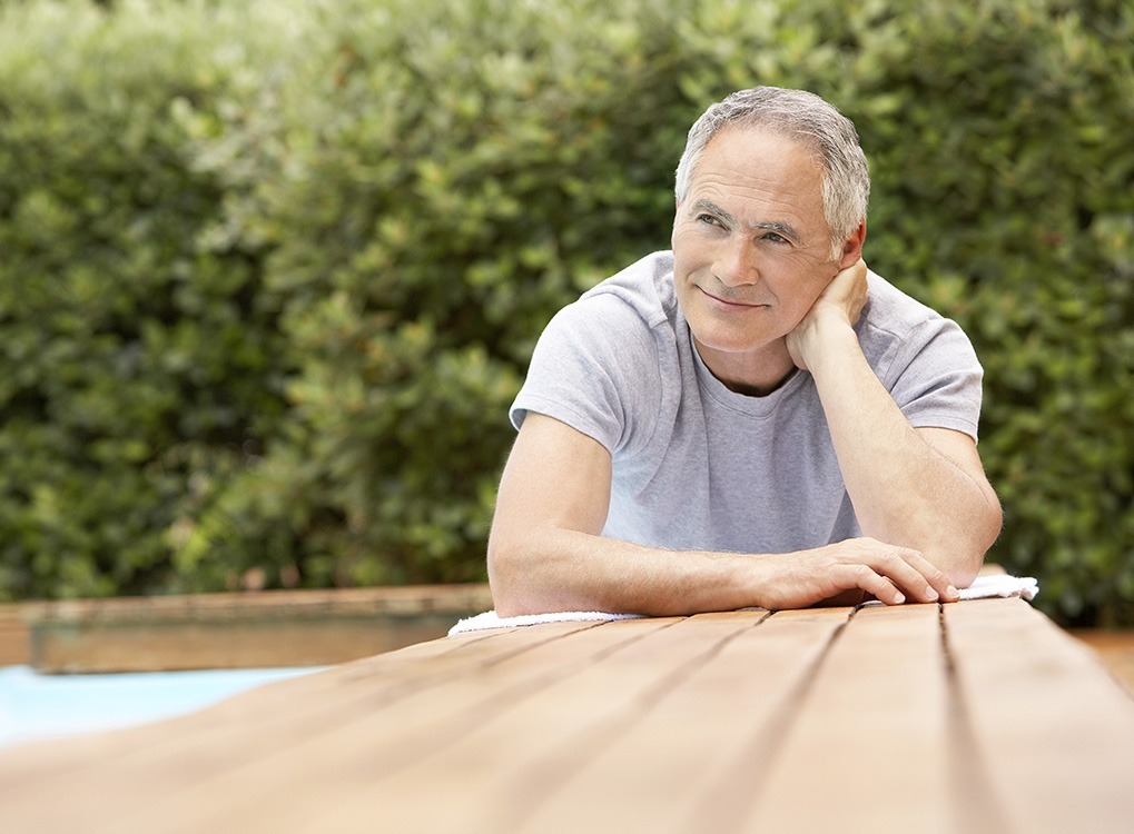 senior white man thinking while sitting on picnic table, with a half smile on his face