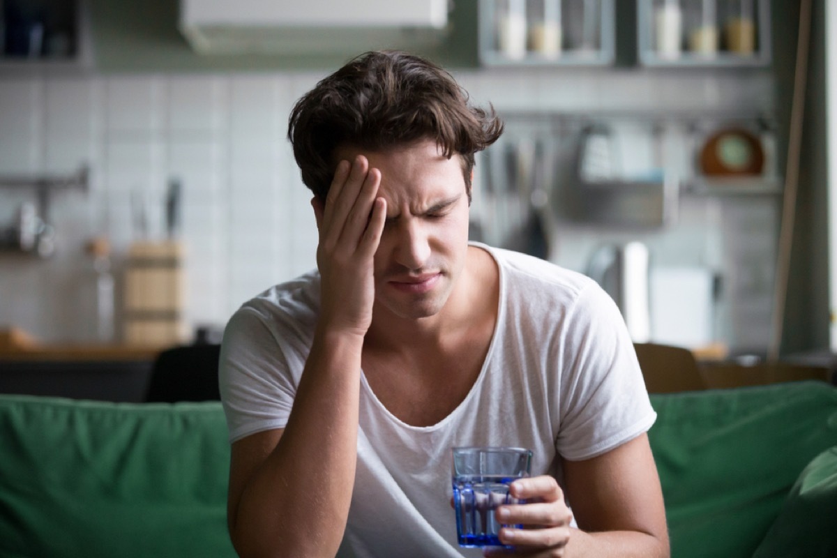 young white man putting his hand on his head and holding a glass of water