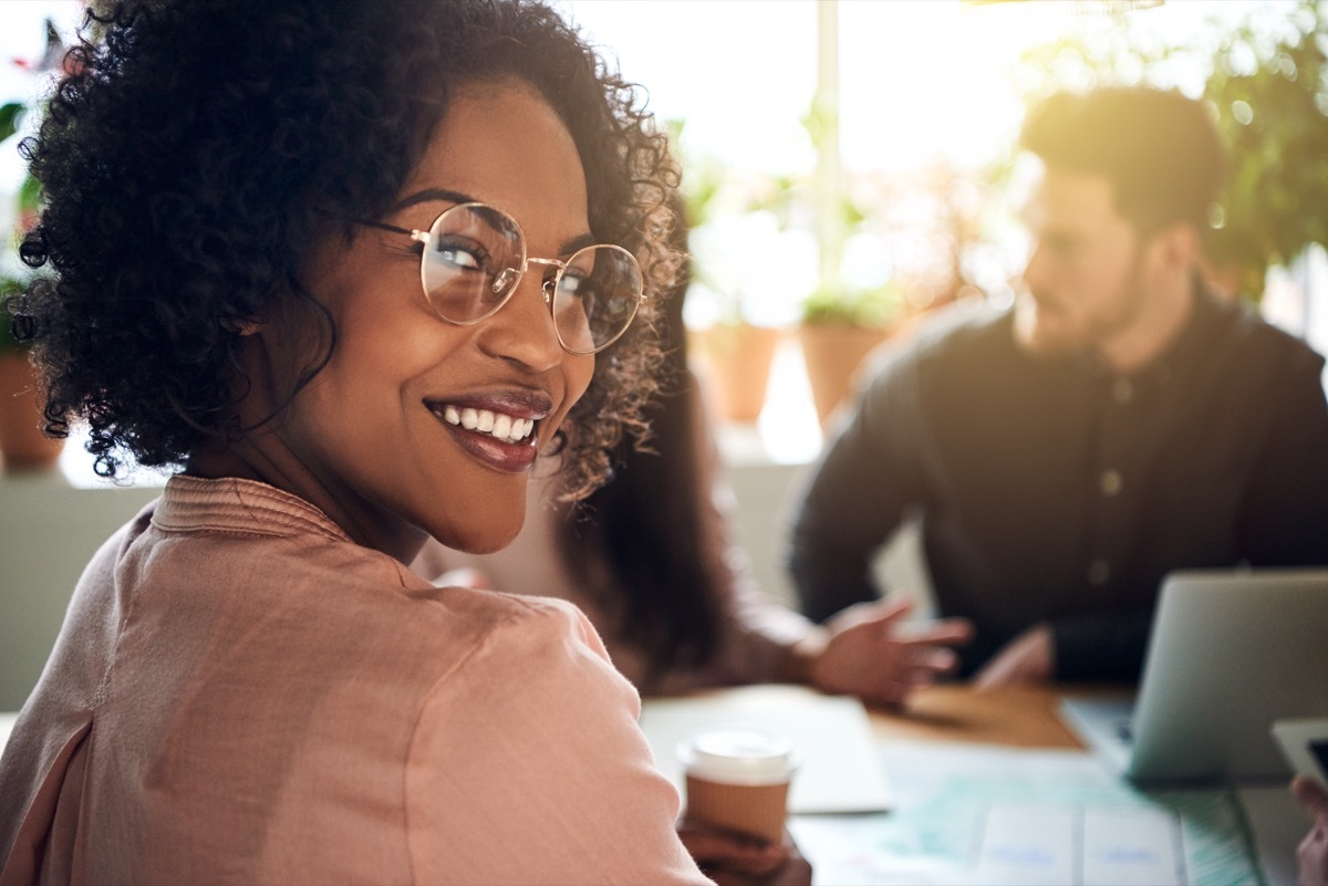 Smiling African businesswoman looking over her shoulder while sitting at a boardroom table with colleagues working in the background