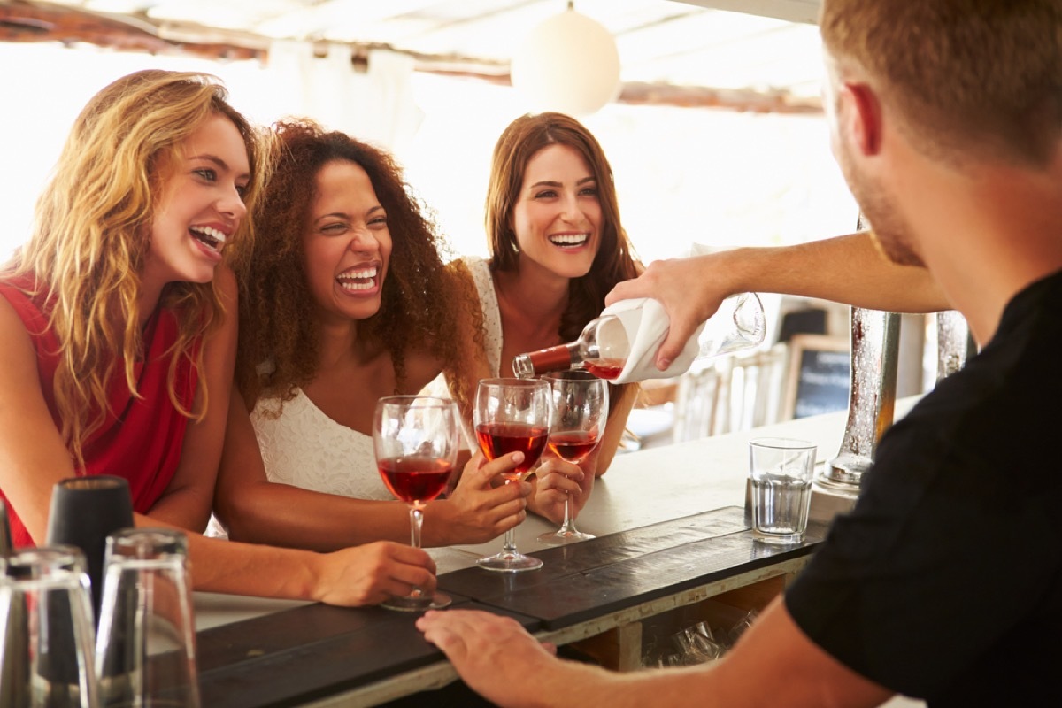 three women with glasses of wine laughing together, female friend