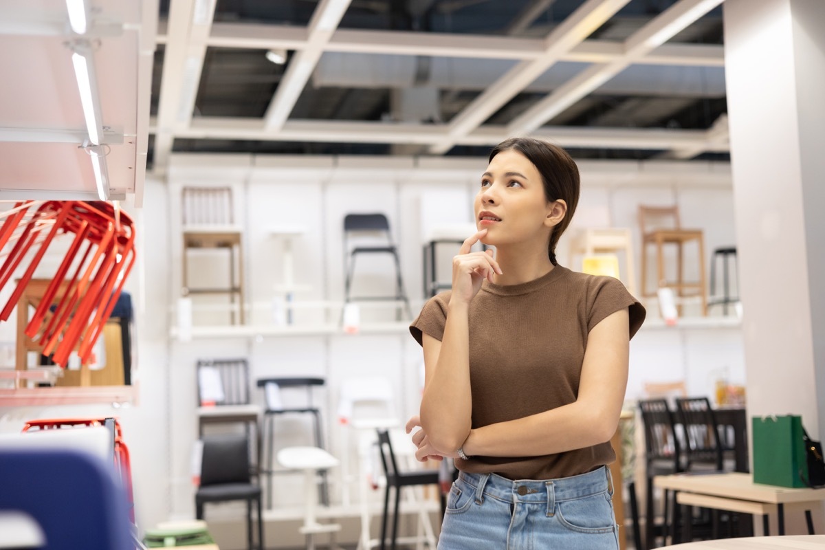 Young beautiful woman choosing the right chair furniture for her house at showroom. Female looking and thinking near lot of armchair at furniture store hall. Buying various item for new house