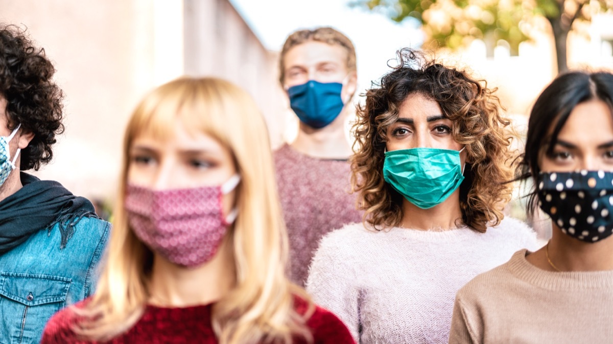 rowd of citizens walking on city street covered by face mask - New normal society concept with young people on worried anxiety mood - Selective focus on bright contrast filter