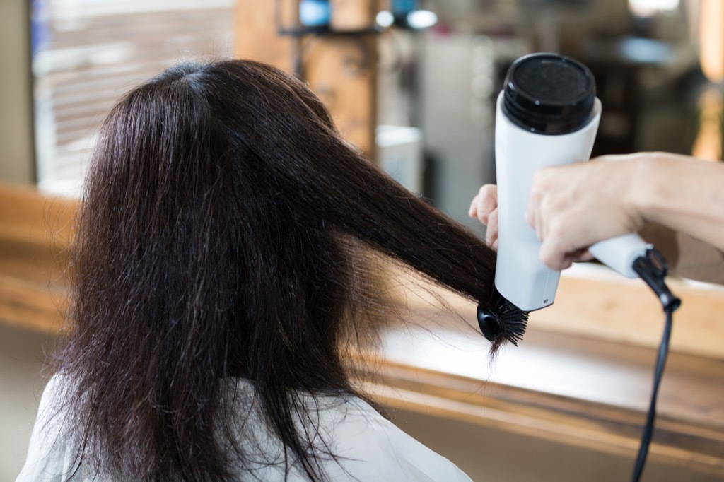 a woman heat-styling her hair - look younger