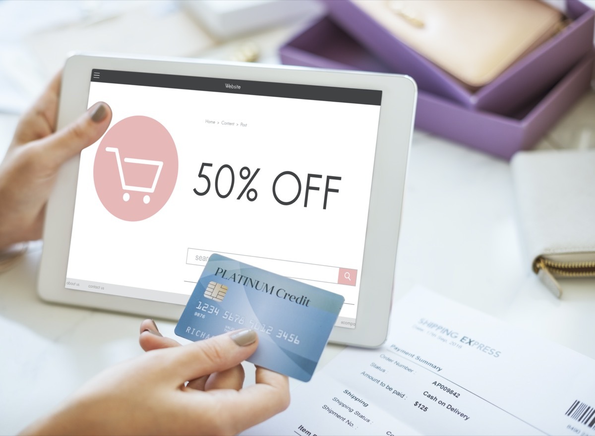 tablet showing a '50% OFF' sign on a website and hand holding a credit card