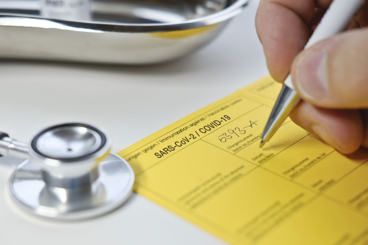 Doctor filling out yellow vaccination card for COVID vaccine