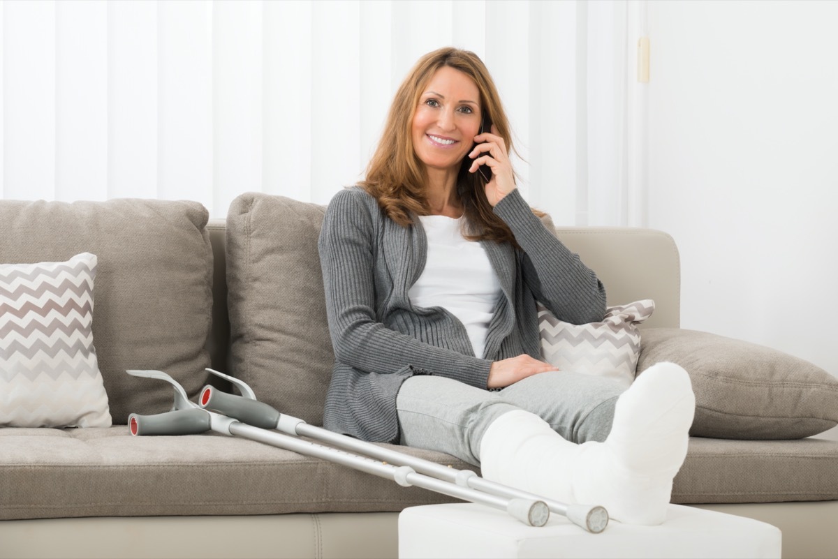 Mature Woman With Plastered Leg Talking On Mobile Phone At Home