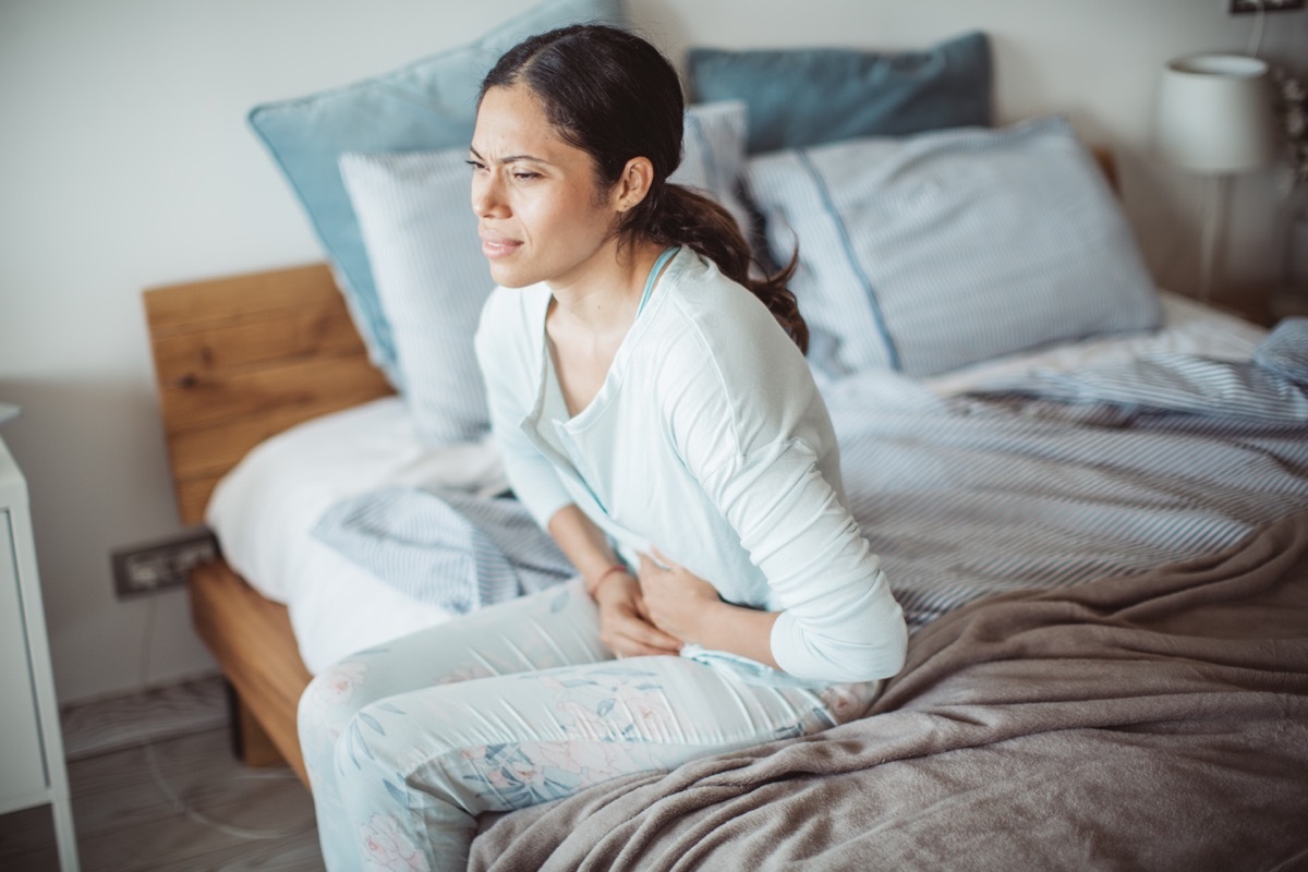 Woman holding her stomach in pain sitting on edge of bed