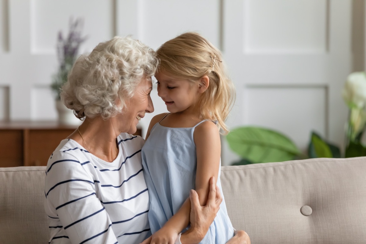 Grandmother hugging her granddaughter while sitting on a couch