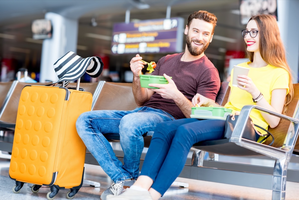 A couple enjoys food while waiting for their plane to arrive. 