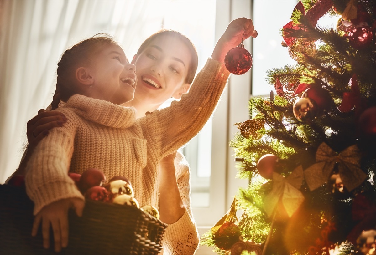 mom and daughter hanging ornaments on a christmas tree