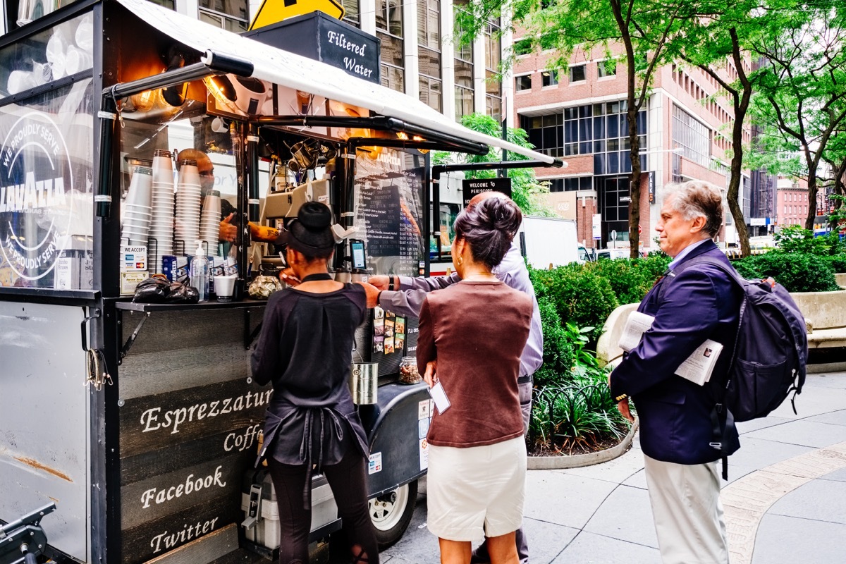 people standing in a line waiting for coffee and bagels from cart