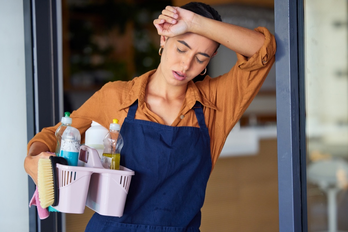 sick woman with headache holding her head and cleaning basket with supplies