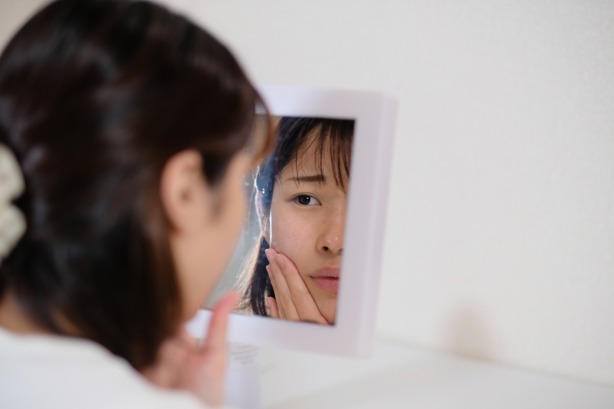 Woman looking at her skin in a mirror. 