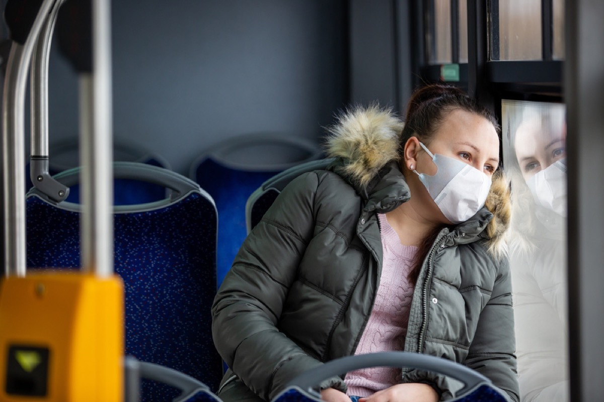 woman with face mask looking out the window on a bus