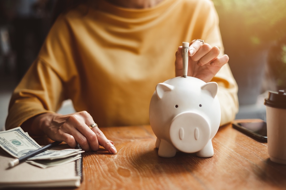 close up of woman putting dollar bills in a piggy bank