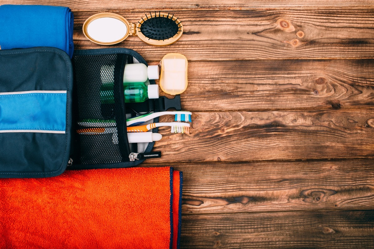 Top view of kit for hygiene during hiking and travel on wooden table with empty space. Items include towel, comb, soap, toothbrushes, shampoo.