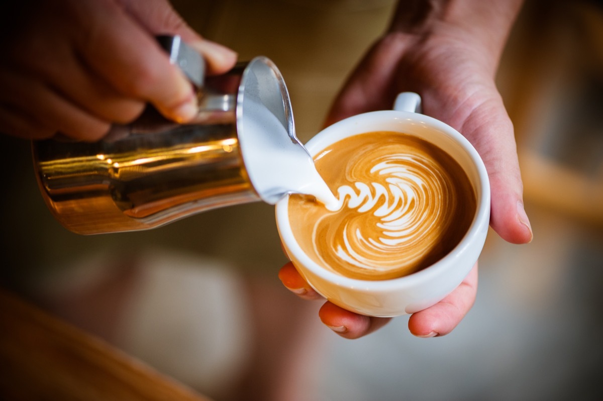 Barista making latte swirl art with golden creamer 