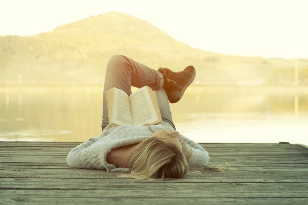 woman relaxing on a dock at sunrise with a book