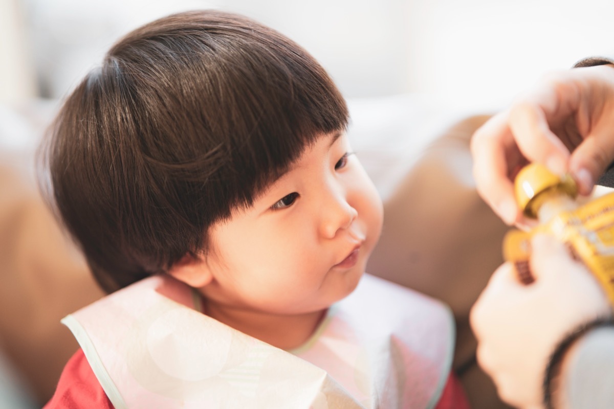 Happy healthy 2 years old Asian toddler looks curious at the snack pouch in her mother's hand, instant healthy nutrition food, selective focus in concept organic baby food for a convenient lifestyle.