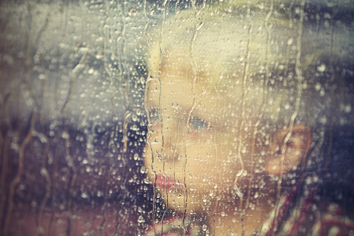 Little boy behind the window in the rain