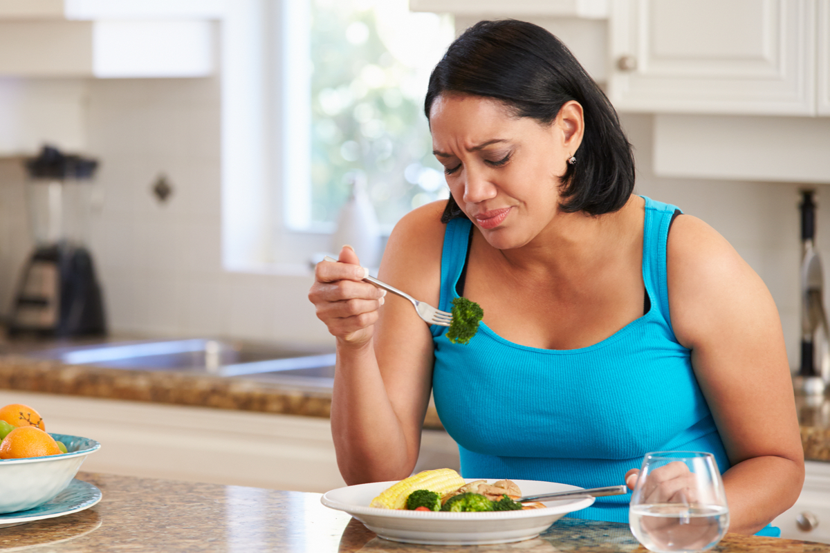 woman eating vegetables and frowning at a piece of broccoli