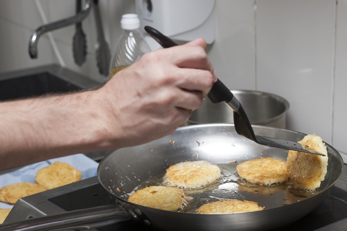 white man frying latkes in silver pan